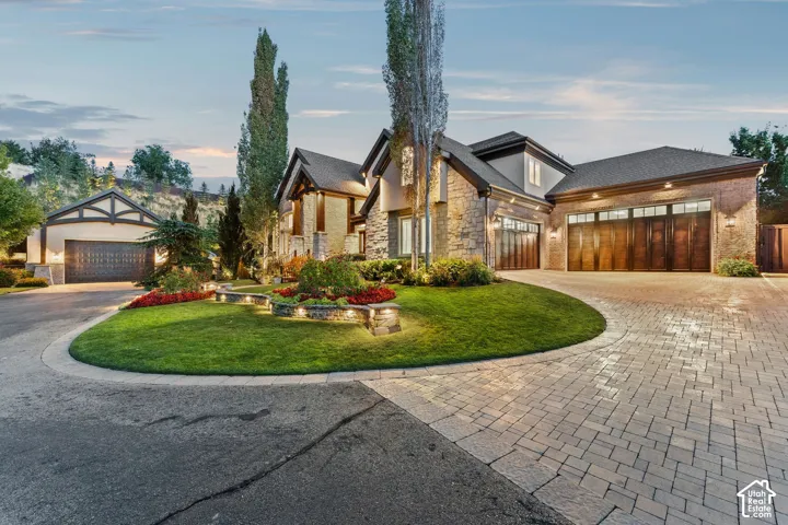 Stone facade with wood-finish garage doors, paver driveway, and landscaped circular lawn