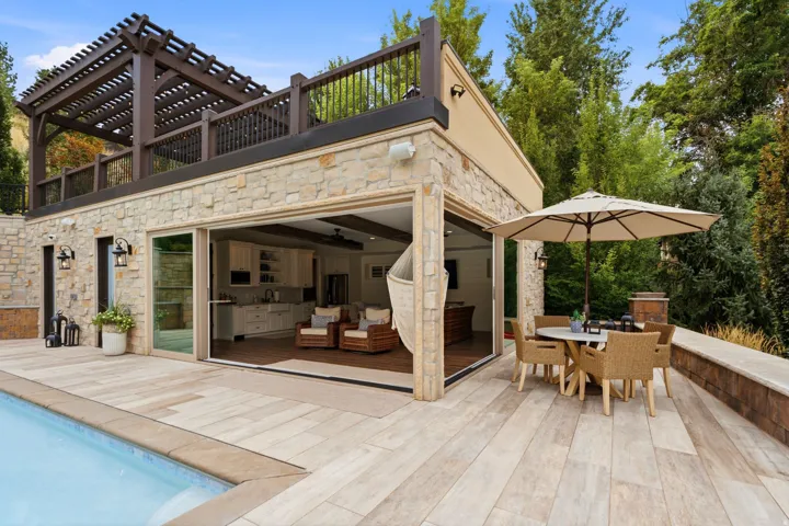 Stone facade with a full-width patio, an integrated pool, and a second-story pergola-covered balcony