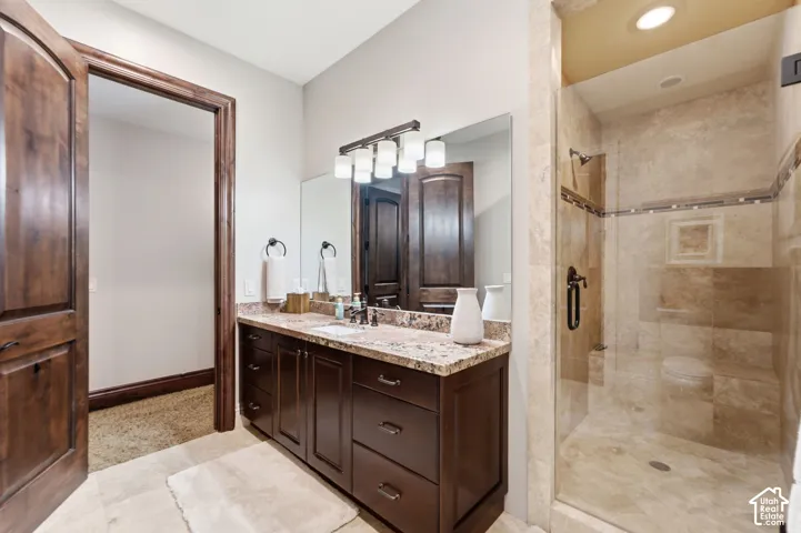 Spacious bathroom featuring a dark wood vanity with a light-toned countertop, a large mirror, a multi-bulb light fixture, and a tiled walk-in shower with a glass enclosure