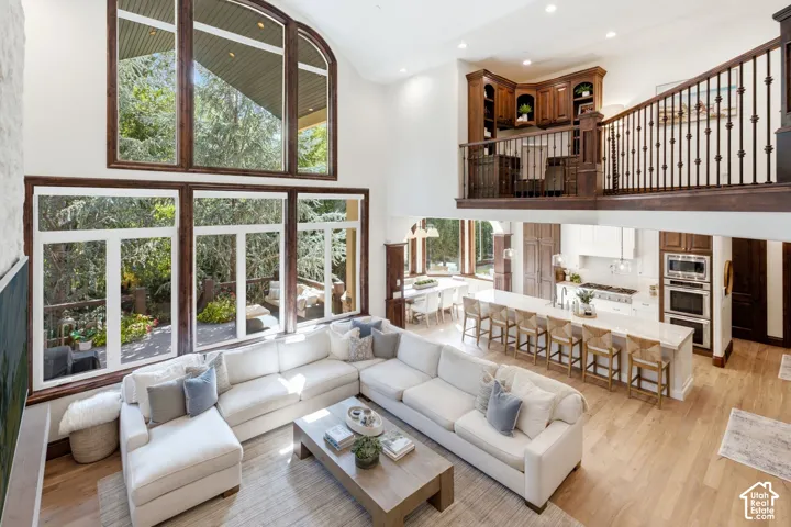 Soaring ceilings with extensive window walls, an open-concept kitchen featuring a large island, stainless steel appliances, and wood-finish flooring throughout