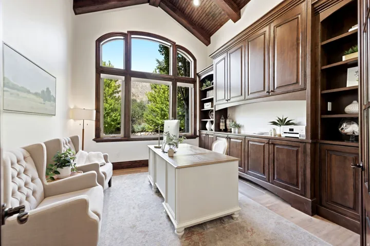 Vaulted wood-paneled ceiling, expansive arched window, built-in dark wood cabinetry, integrated shelving, and light-toned flooring