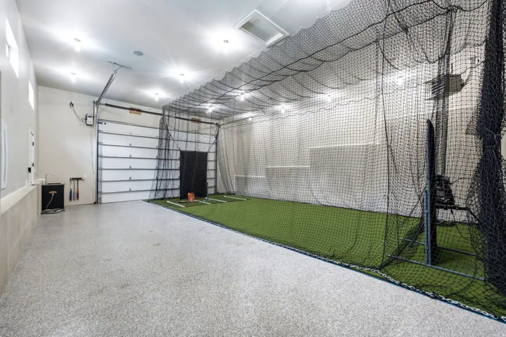 Indoor sports facility featuring a batting cage, artificial turf flooring, and a roll-up garage door