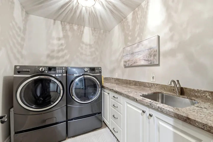 Built-in cabinetry with white shaker-style doors, stone-finish countertop, and undermount stainless steel sink with a gooseneck faucet