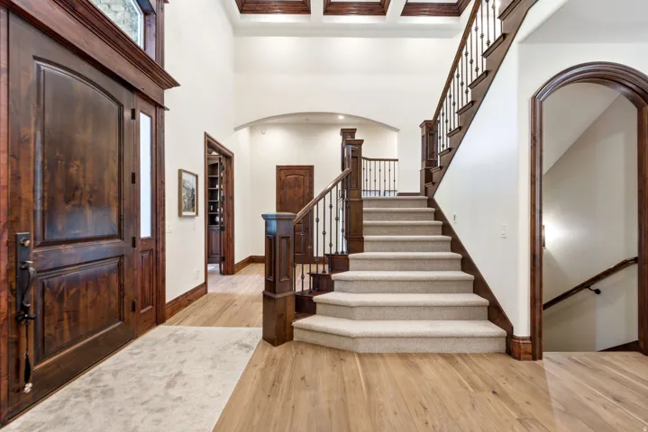 Grand entryway featuring a two-story ceiling, wood-finish flooring, a substantial wood staircase with wrought iron balusters, and a solid wood entry door with an arched transom
