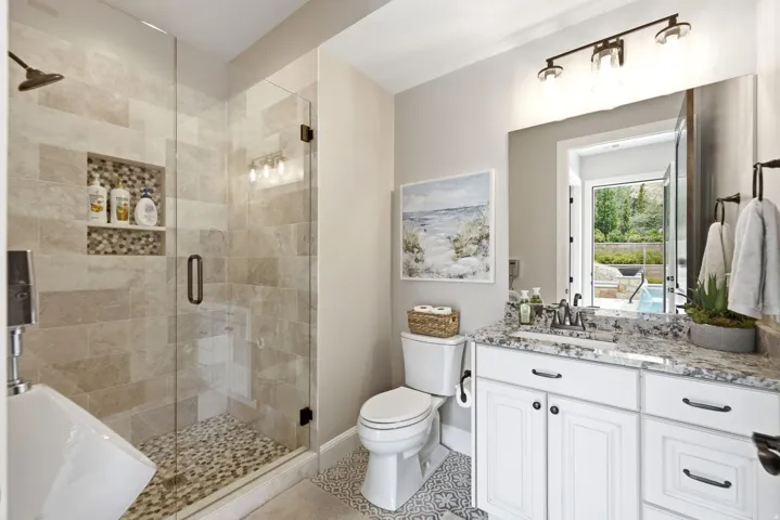 Walk-in shower with natural stone tile surround and mosaic floor, glass enclosure, white vanity with stone countertop, and decorative floor tile