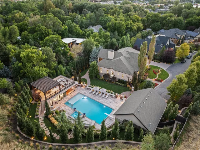 Spacious property featuring a large swimming pool, an elevated outdoor living area with a pergola, a separate outbuilding, a circular driveway, and extensive perimeter landscaping