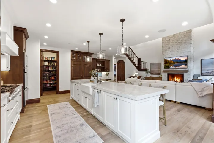 Spacious kitchen featuring a large central island with a farmhouse sink, light wood-finish flooring, and a walk-in pantry
