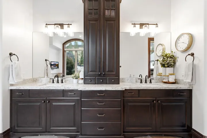 Dual vanity featuring dark wood cabinetry, light-toned countertops, and two wall-mounted light fixtures
