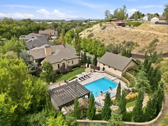 Expansive property featuring a large swimming pool, integrated spa, adjacent pool house, and a pergola-covered patio area