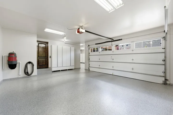 Spacious garage with light gray speckled flooring, white cabinetry, and a dark wood-finish interior door
