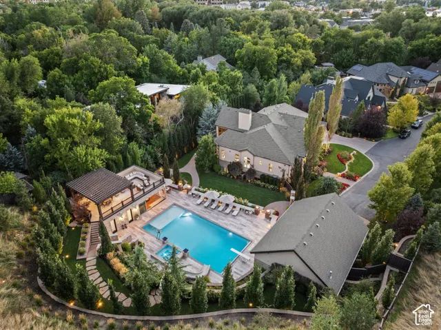 Spacious property featuring a large swimming pool, an elevated outdoor living area with a pergola, a separate outbuilding, a circular driveway, and extensive perimeter landscaping