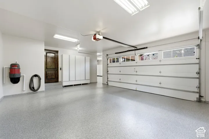 Spacious garage with light gray speckled flooring, white cabinetry, and a dark wood-finish interior door