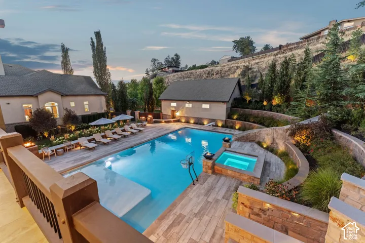 Expansive swimming pool with integrated spa, wood-finish decking, terraced landscaping with stone retaining walls, and a detached auxiliary building