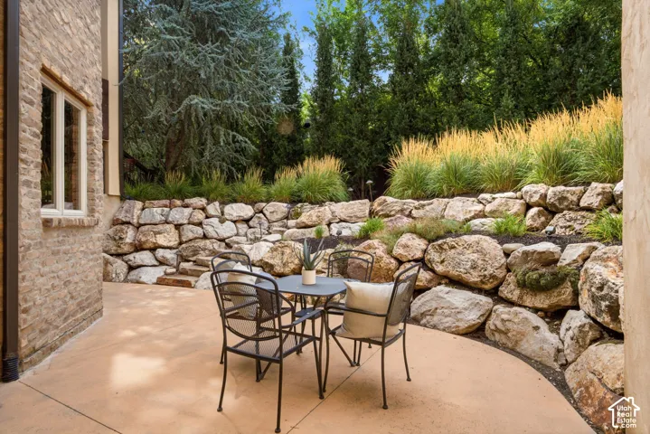 Stone retaining walls with integrated plantings, expansive concrete patio, and a brick exterior facade