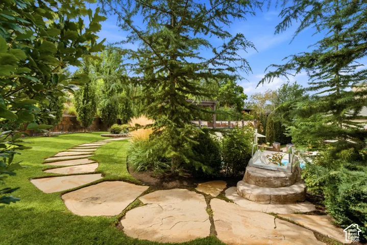 Expansive lawn with a natural stone pathway, mature trees, diverse plantings, and a stone-clad water feature
