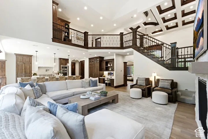 Vaulted ceiling with exposed wood beams, wood-finish flooring, staircase with wrought iron balusters, recessed lighting, and a stone fireplace