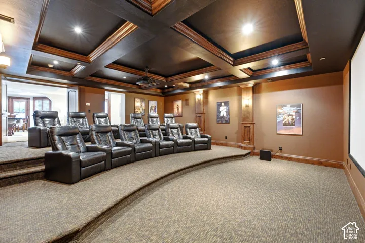 Dedicated theater room with tiered seating, recessed lighting, coffered ceiling detail, wall sconces, and a large projection screen