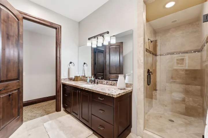 Spacious bathroom featuring a dark wood vanity with a light-toned countertop, a large mirror, a multi-bulb light fixture, and a tiled walk-in shower with a glass enclosure