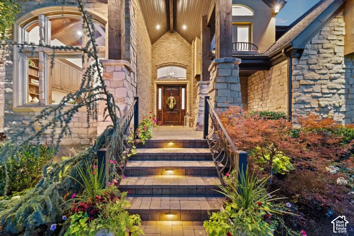 Stone facade exterior featuring an arched wood-finish entry door, paver stone walkway with integrated lighting, and decorative metal railings