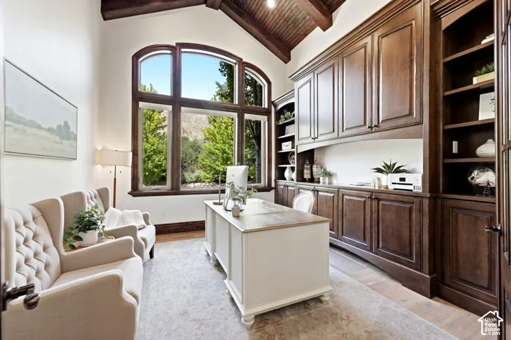 Vaulted wood-paneled ceiling, expansive arched window, built-in dark wood cabinetry, integrated shelving, and light-toned flooring