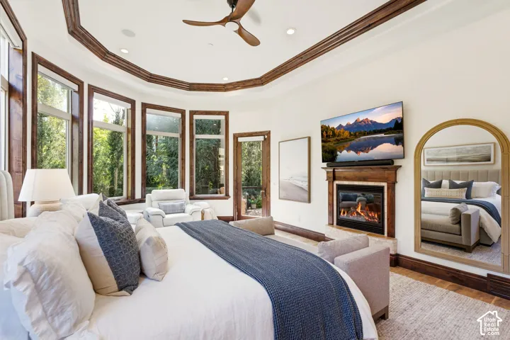Recessed ceiling with wood trim, built-in fireplace, wood-finish flooring, multiple pane windows, and a ceiling fan