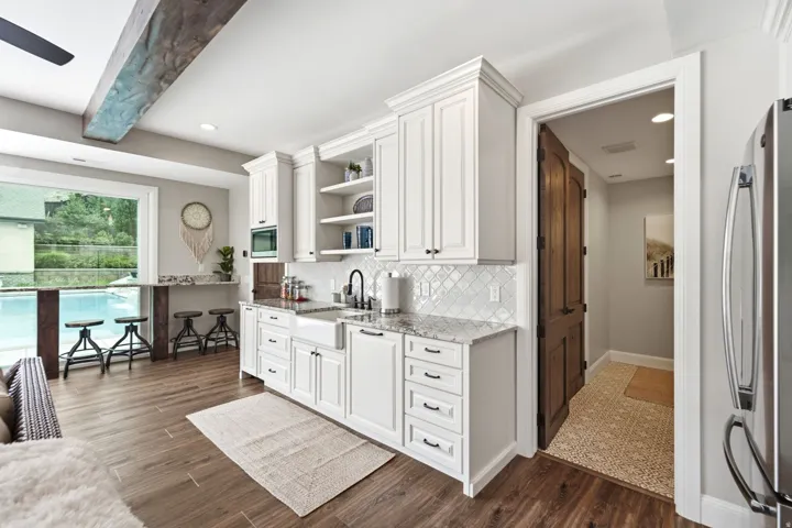 Casita -White shaker-style cabinetry with crown molding, granite countertops, a white apron-front sink, and a diamond-patterned tile backsplash