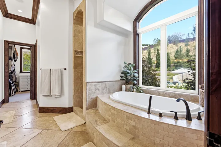 Deep soaking tub with dark bronze fixtures, set against an arched picture window