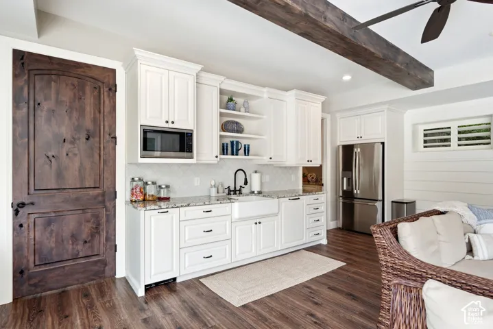 White cabinetry with open shelving, integrated microwave, stainless steel refrigerator, farmhouse sink, and wood-finish flooring