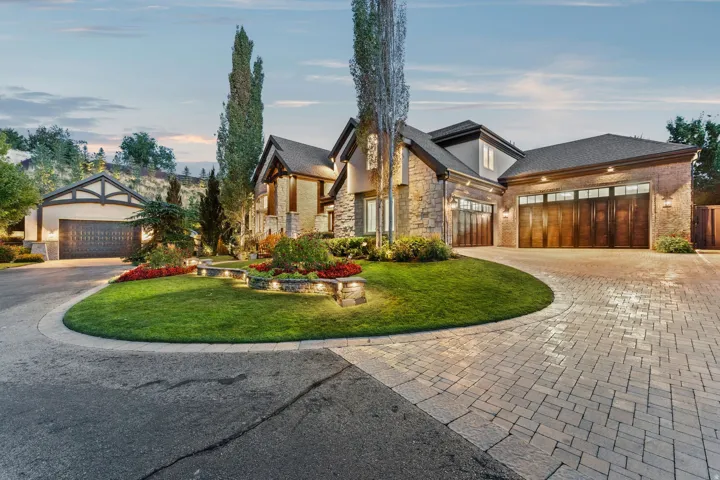 Stone facade with wood-finish garage doors, paver driveway, and landscaped circular lawn