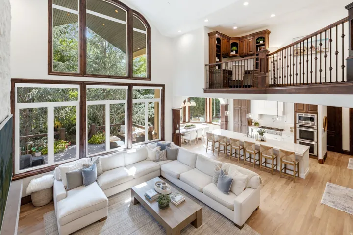 Soaring ceilings with extensive window walls, an open-concept kitchen featuring a large island, stainless steel appliances, and wood-finish flooring throughout