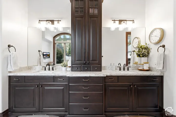 Dual vanity featuring dark wood cabinetry, light-toned countertops, and two wall-mounted light fixtures