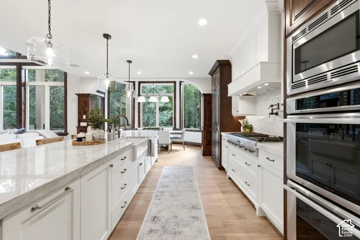 Expansive kitchen island with a stone countertop, white shaker cabinetry, stainless steel appliances, and wood-finish flooring