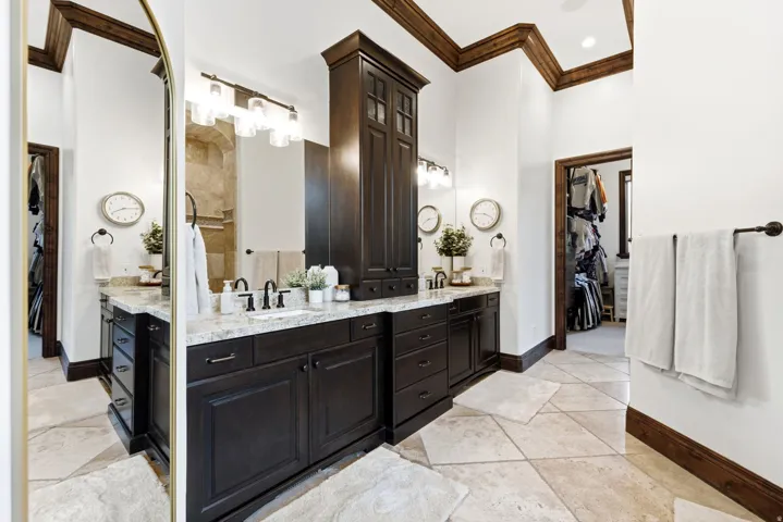 Dual vanity with stone countertops and undermount sinks, dark wood-finish cabinetry, and decorative crown molding
