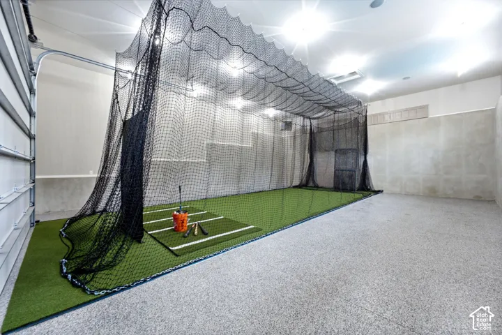 Indoor batting cage with artificial turf, overhead lighting, and a roll-up garage door