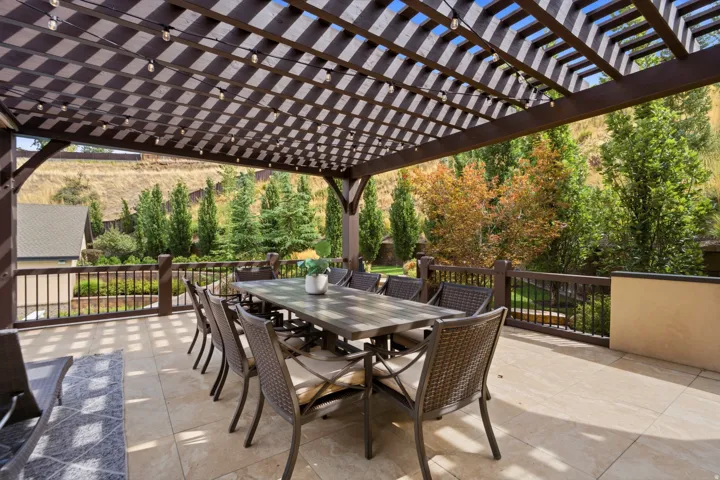 Expansive outdoor patio featuring a slatted pergola, decorative string lighting, tiled flooring, and a perimeter railing
