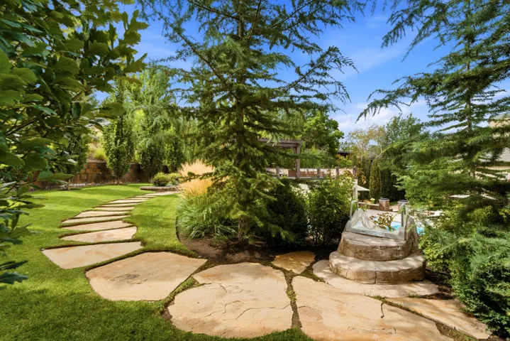 Expansive lawn with a natural stone pathway, mature trees, diverse plantings, and a stone-clad water feature