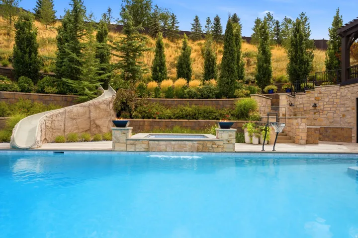 Resort-style pool with a rock-feature slide, integrated spa, and stone-clad retaining walls