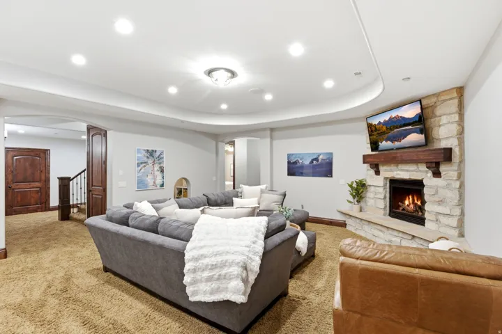 Stone-clad fireplace with wood mantel, recessed ceiling lighting, and arched doorways