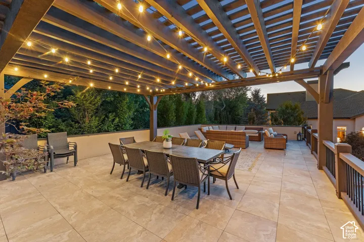 Expansive outdoor patio featuring a wooden pergola, string lighting, and tile flooring