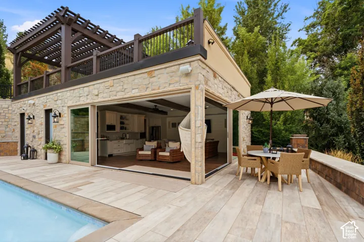 Stone facade with a full-width patio, an integrated pool, and a second-story pergola-covered balcony