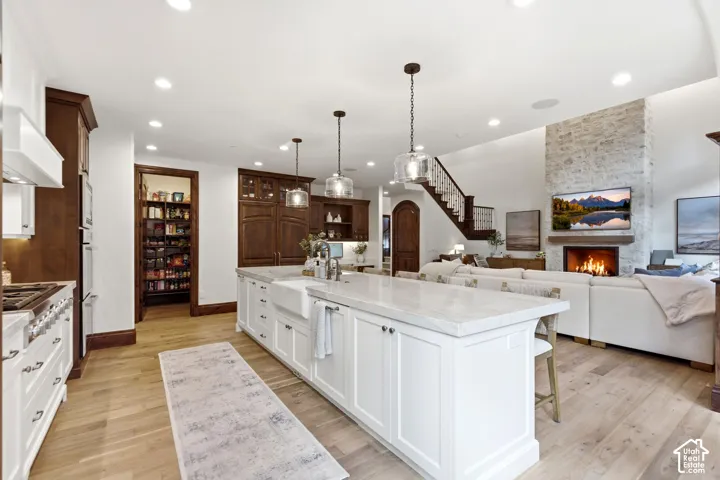 Spacious kitchen featuring a large central island with a farmhouse sink, light wood-finish flooring, and a walk-in pantry