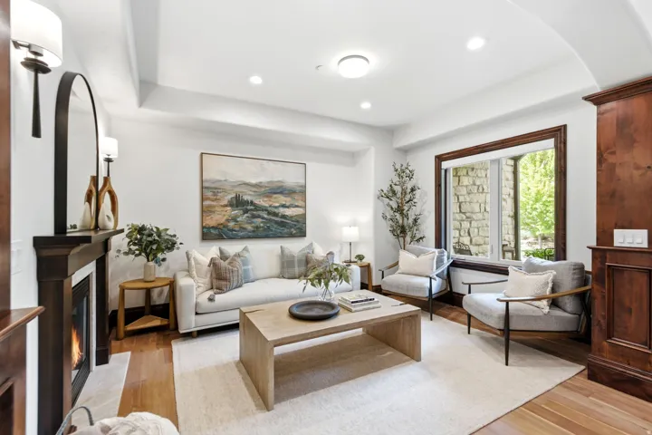 Living area featuring rich wood-finish flooring, a built-in fireplace with a mantel, recessed lighting, and a window with wood trim