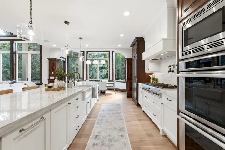 Expansive kitchen island with a stone countertop, white shaker cabinetry, stainless steel appliances, and wood-finish flooring