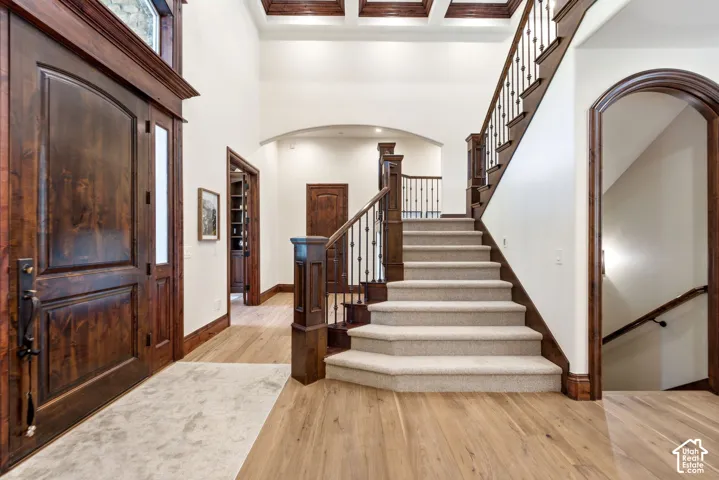Grand entryway featuring a two-story ceiling, wood-finish flooring, a substantial wood staircase with wrought iron balusters, and a solid wood entry door with an arched transom