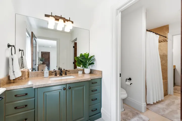 Primary bathroom featuring a dual-sink vanity with wood-finish countertop, teal cabinetry with bronze hardware, large framed mirror, and integrated lighting fixture