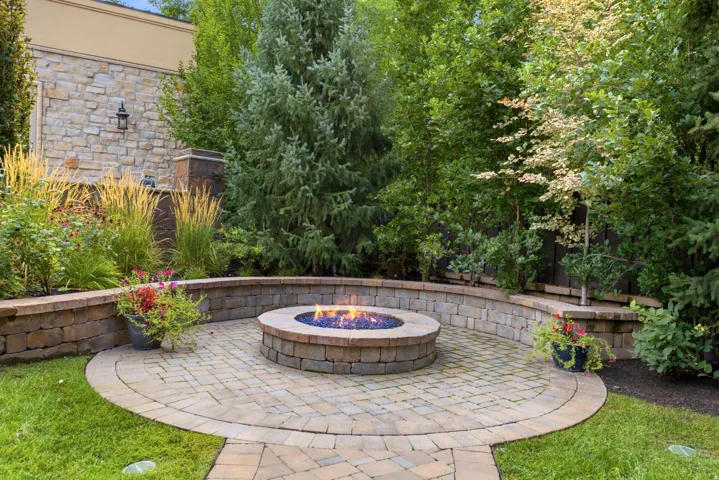 Paver patio featuring a built-in fire pit, surrounded by a stone retaining wall with integrated landscaping