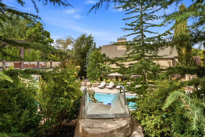 In-ground swimming pool with an integrated slide feature, surrounded by mature landscaping and a multi-level deck