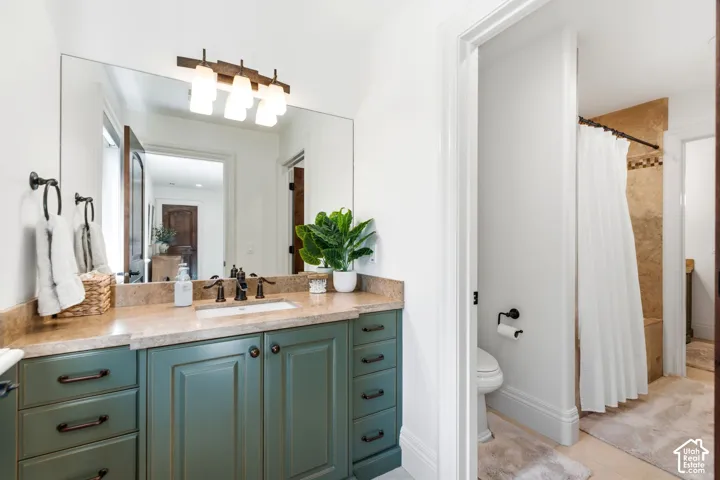 Primary bathroom featuring a dual-sink vanity with wood-finish countertop, teal cabinetry with bronze hardware, large framed mirror, and integrated lighting fixture