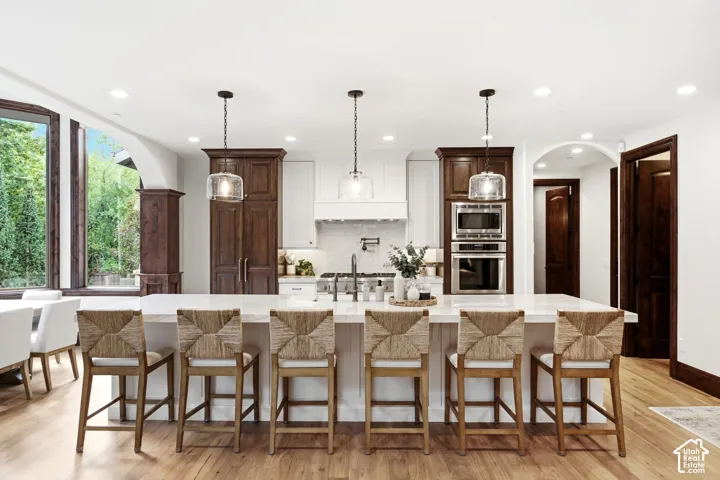 Kitchen featuring a large central island, recessed lighting, wood-finish flooring, stainless steel built-in appliances, and a tiled backsplash