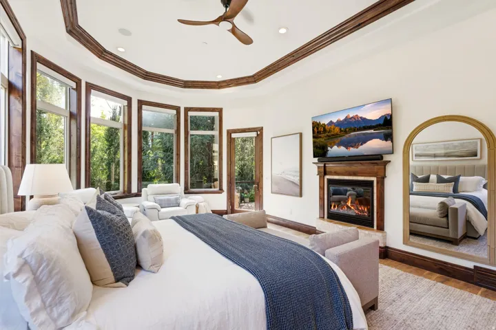 Recessed ceiling with wood trim, built-in fireplace, wood-finish flooring, multiple pane windows, and a ceiling fan
